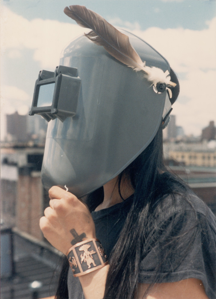 A person wearing a protective mask with feathers, showcasing a tattoo on their wrist.