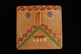 Ceramic tile with a stylized face, featuring blue eyes and colorful decorative lines.